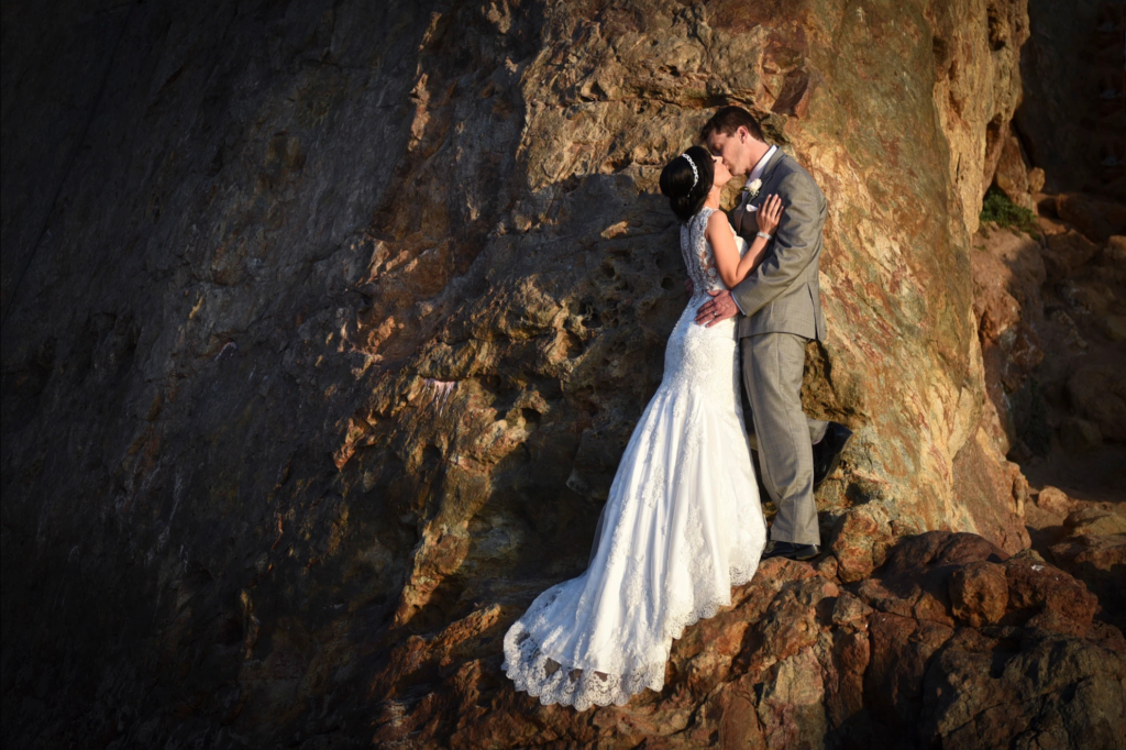Bride and groom embracing on a sunlit cliffside