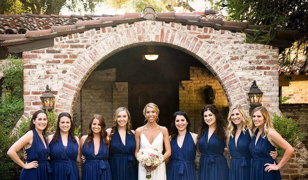 Bride and bridesmaids in navy gowns under a brick archway