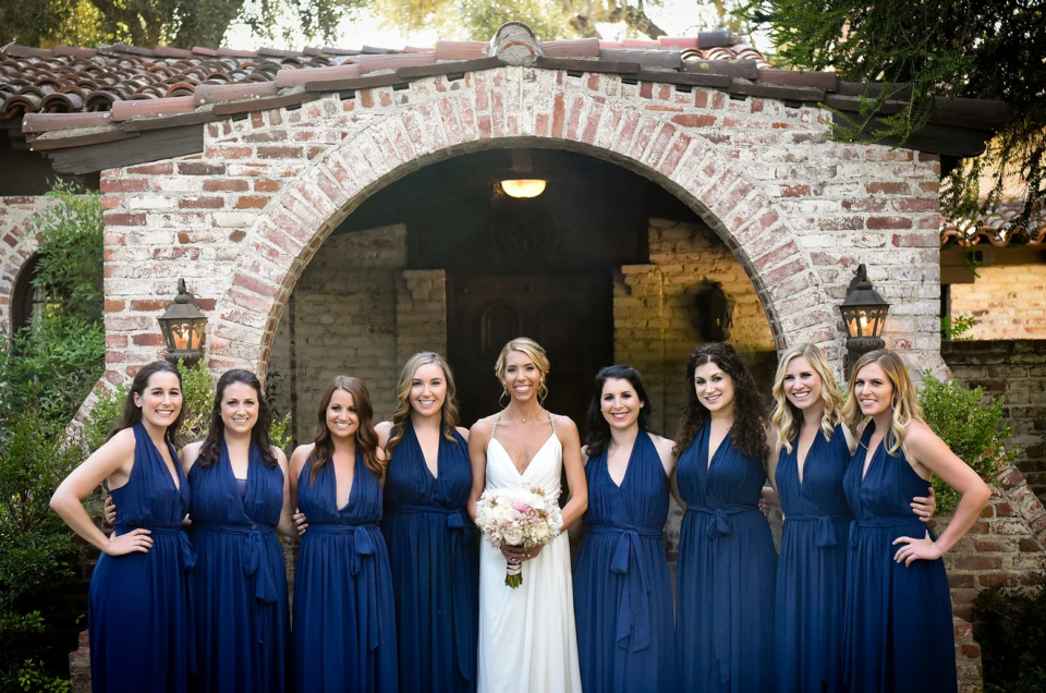 Bride and bridesmaids in navy gowns under a brick archway