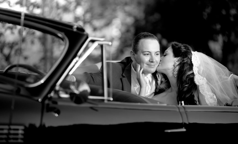 Bride kissing groom in a vintage convertible, black and white