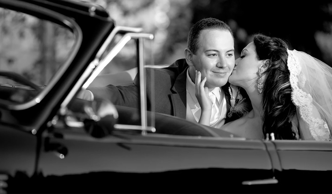 Bride kissing groom in a vintage convertible, black and white